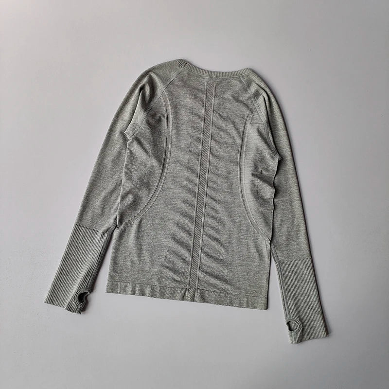 Grey seamless long-sleeve sports top with ribbed cuffs, thumb holes, and contour detailing on the back.