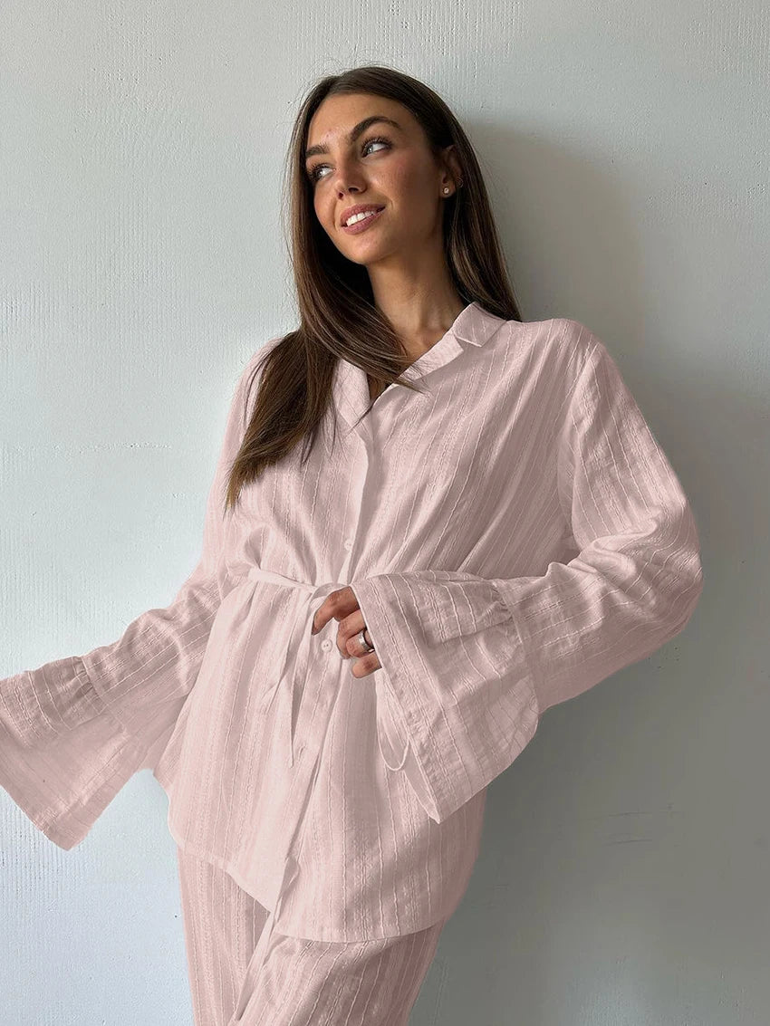 Model wearing a light pink, textured button-up shirt with a tie waist and flared sleeves.