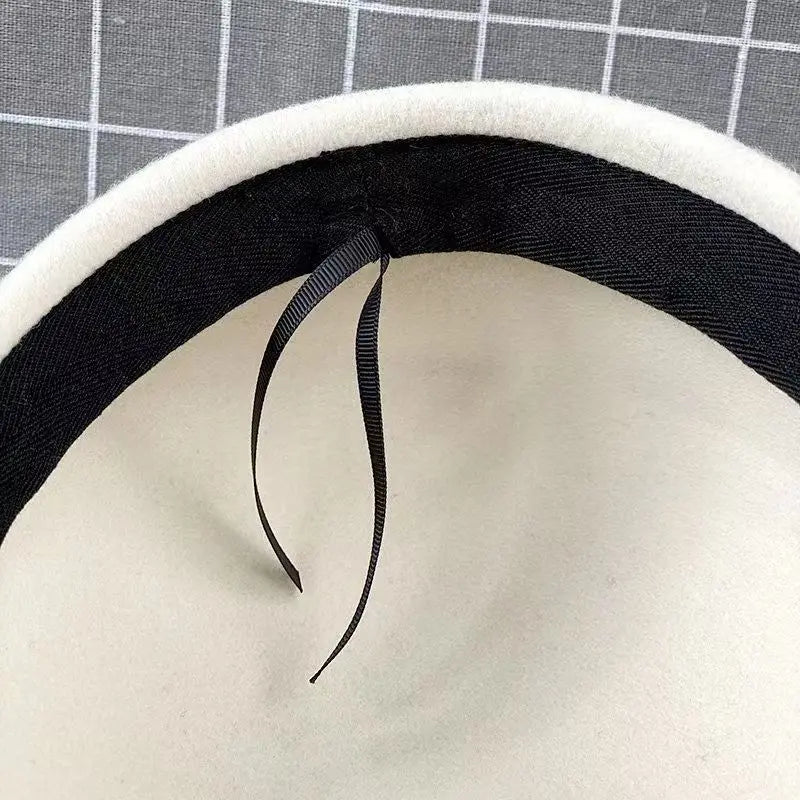 Close-up of the interior of a cream wool felt beret, featuring a black inner lining and adjustable ribbon tie.