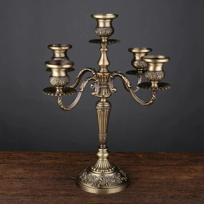 Bronze metal 5-arm candelabra with floral embossed details on the base and candle cups, standing on a wooden table.