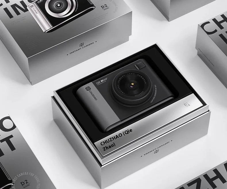 Black and grey plastic instant camera with central lens in a branded rectangular product display box.