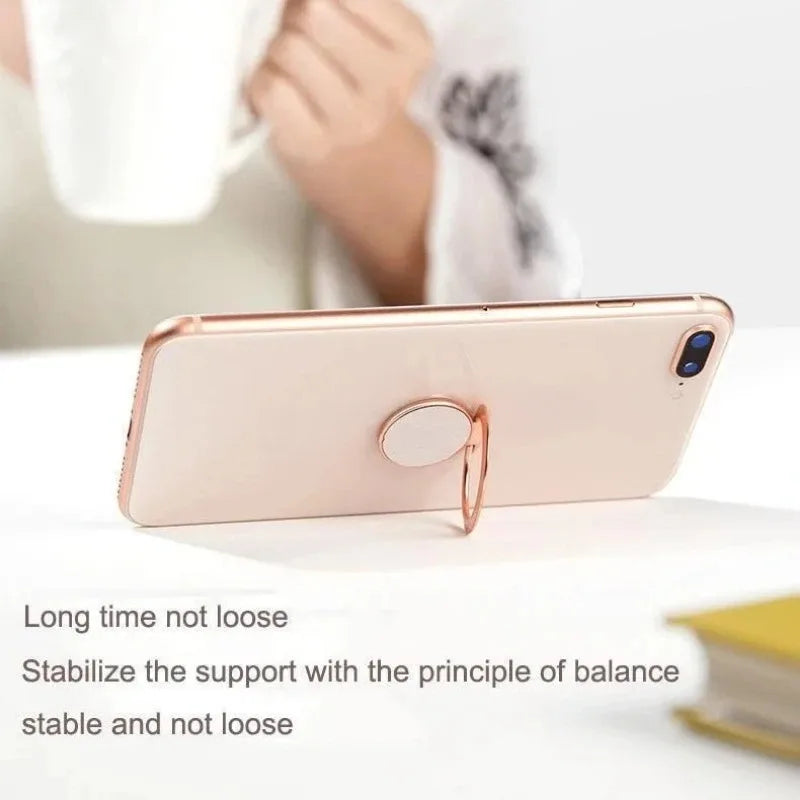 A rose gold circular phone ring holder attached to the back of a smartphone, acting as a stand on a white surface.