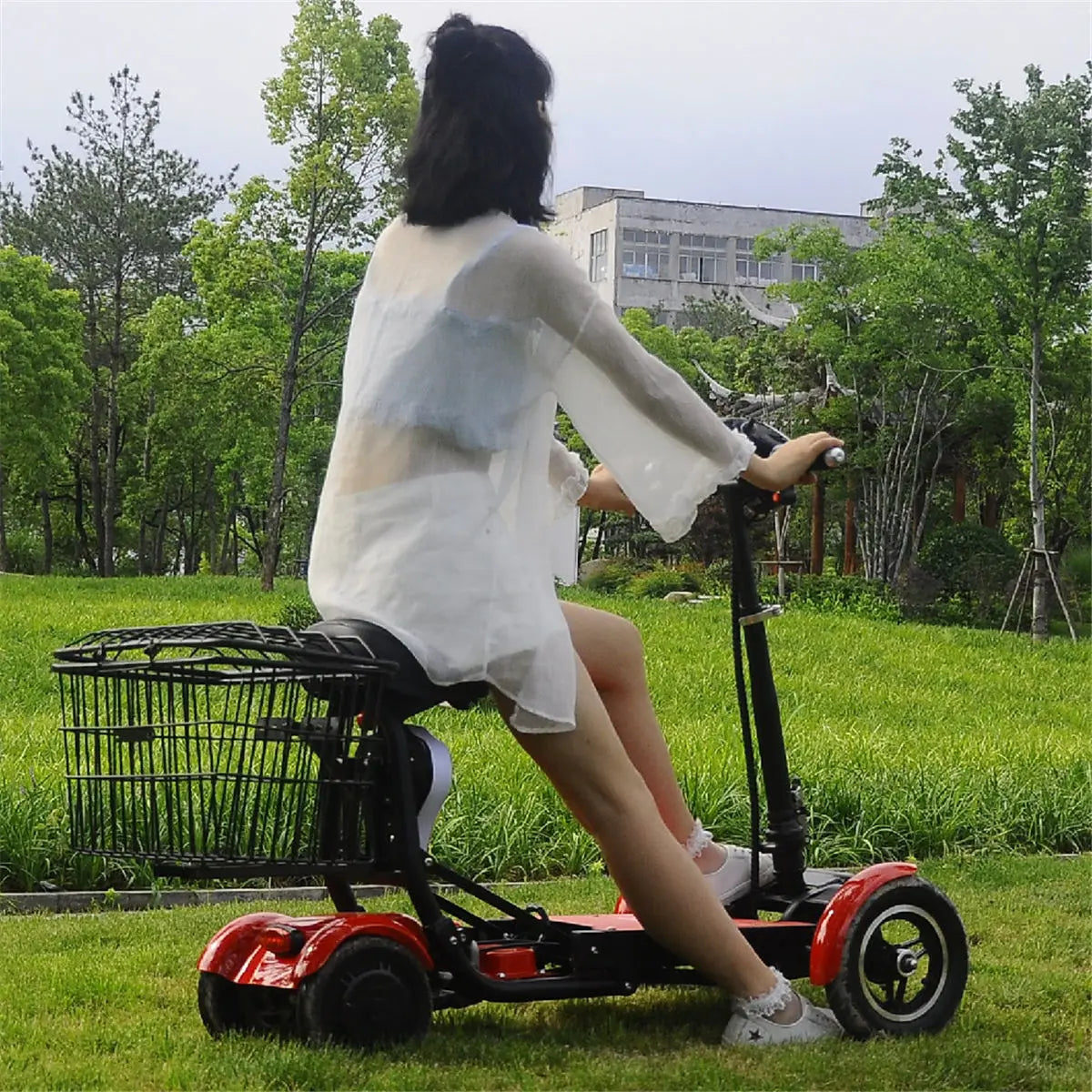 Red 4-wheel electric mobility scooter with dual seats, handlebars, and a black rear storage basket on a grassy lawn.