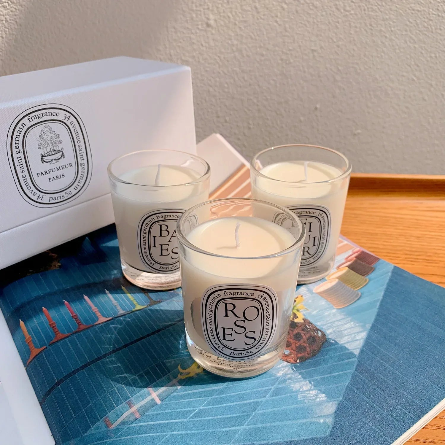 Three white wax scented candles in clear glass tumblers with oval labels, displayed with a white gift box.