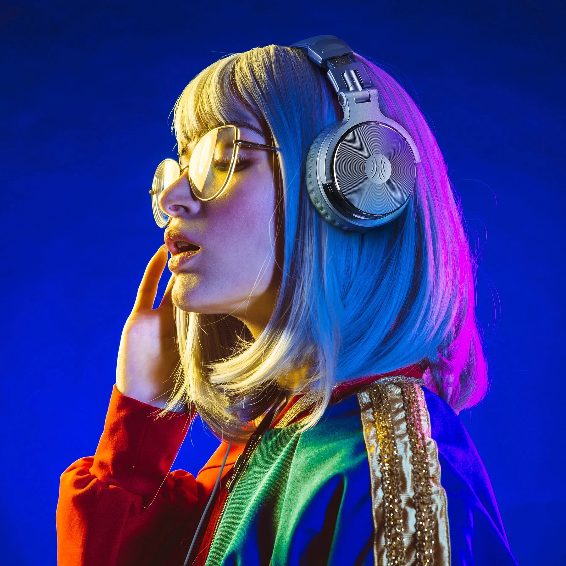 A person wearing sleek silver, professional wired studio headphones against a vibrant neon blue background.