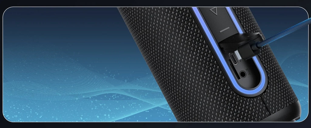 Close-up of a black fabric Bluetooth speaker with blue LED light accents, being charged via a USB-C cable.