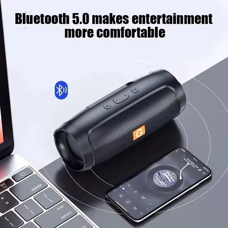A black cylindrical wireless Bluetooth speaker with top-mounted buttons, sitting on a desk next to a smartphone.
