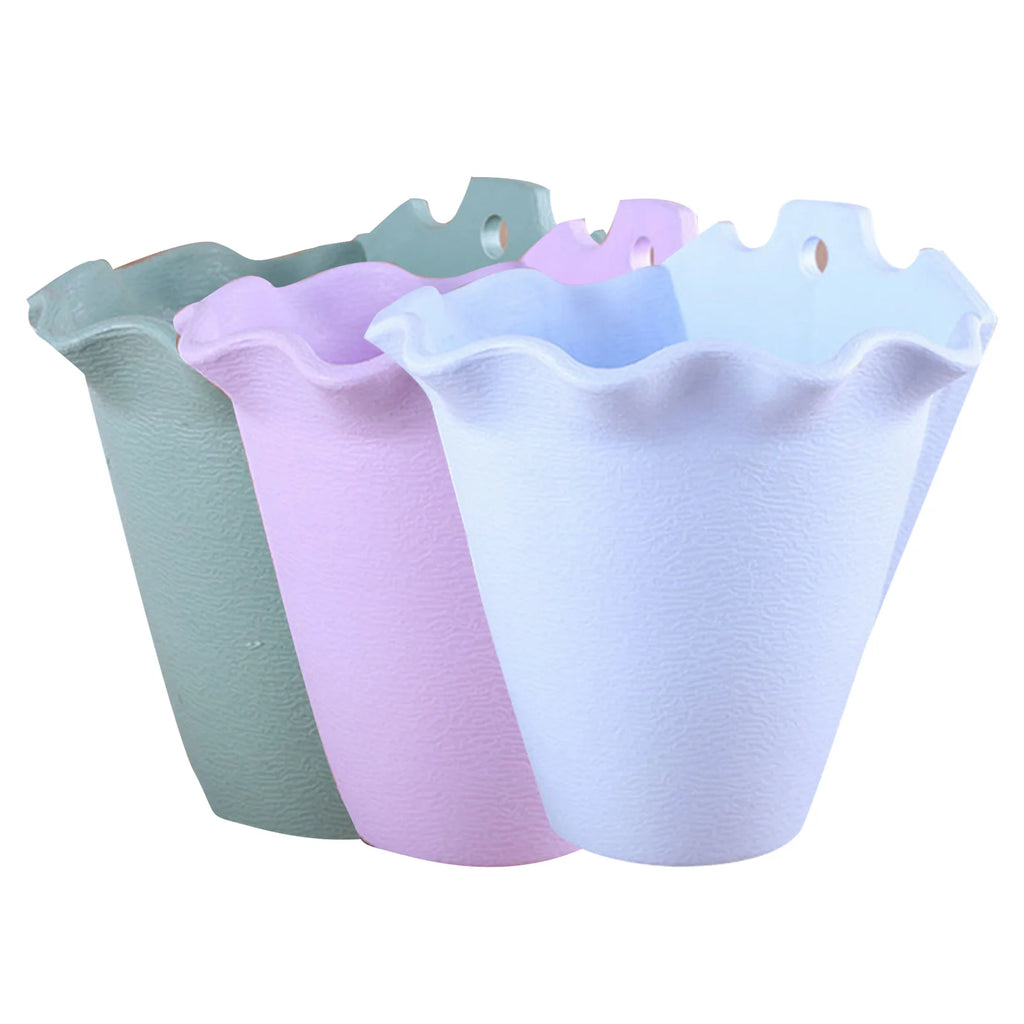 Three textured, wall-hanging plastic planters in sage green, soft pink, and light blue with scalloped edges.
