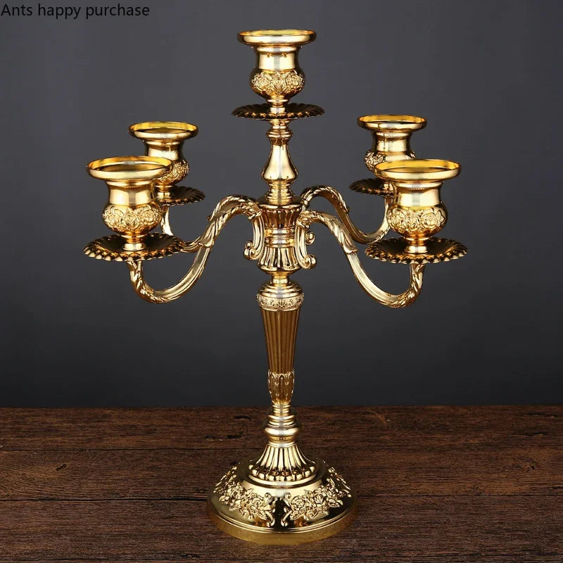 Gold 5-arm candelabra with ornate floral embossing on candle cups and base, standing on a dark wooden surface.