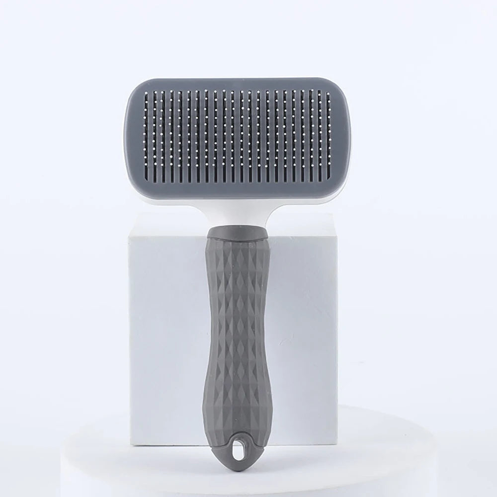 Grey and white self-cleaning slicker brush for pets with a textured, ergonomic handle, standing on a white pedestal.