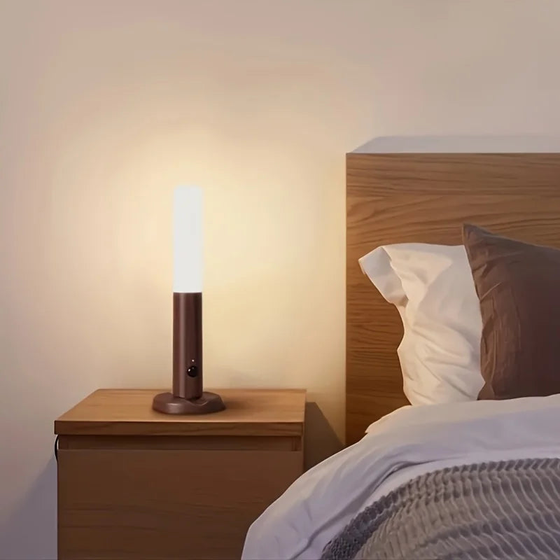 Slim, cylindrical rechargeable LED night light with motion sensor, featuring a warm glow on a wooden bedside table.