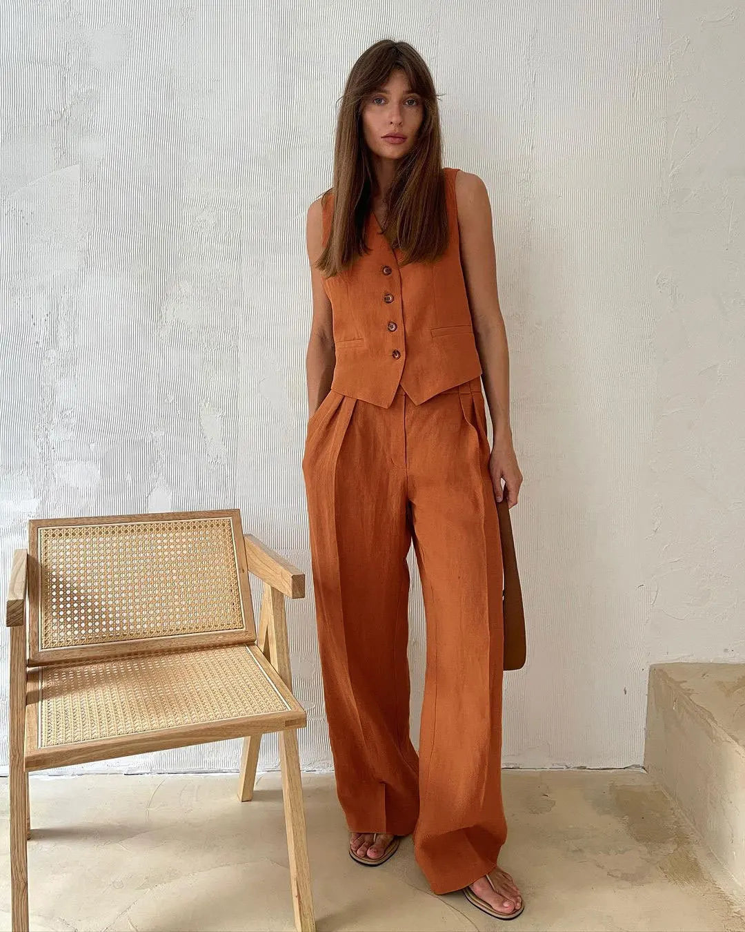 Model wearing a burnt orange linen-style vest with button-front closure and matching wide-leg pleated trousers.