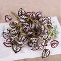 Artificial plant branch with dark purple oval leaves featuring striking white striped patterns on a white paper background.