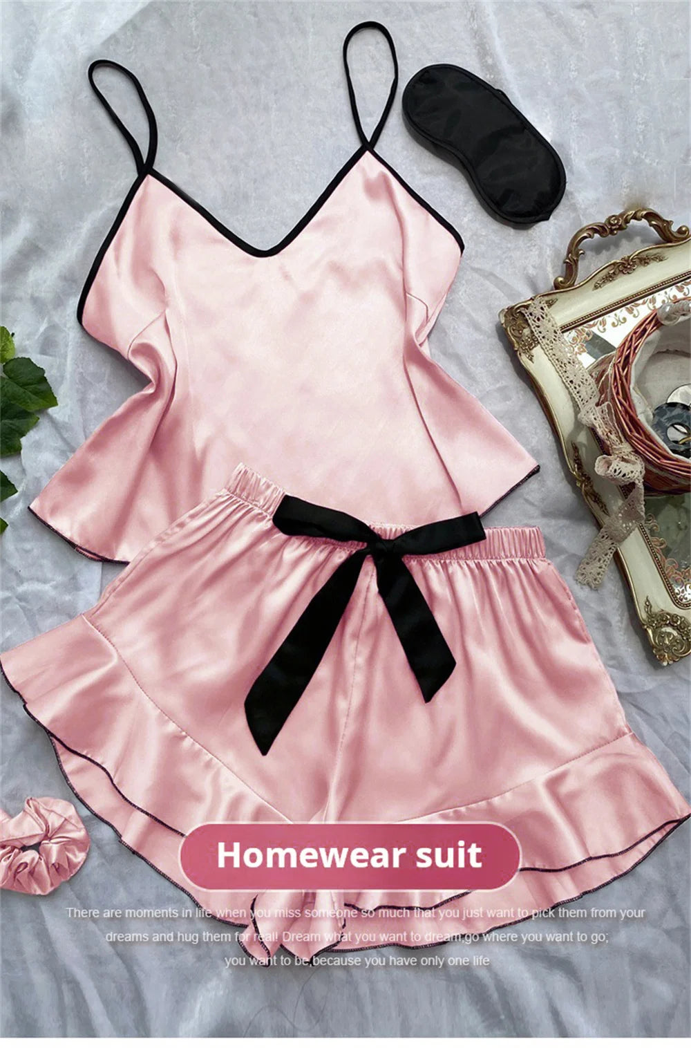 Pink satin camisole and ruffle-hem shorts pyjama set with black trim, matching eye mask, and scrunchie.