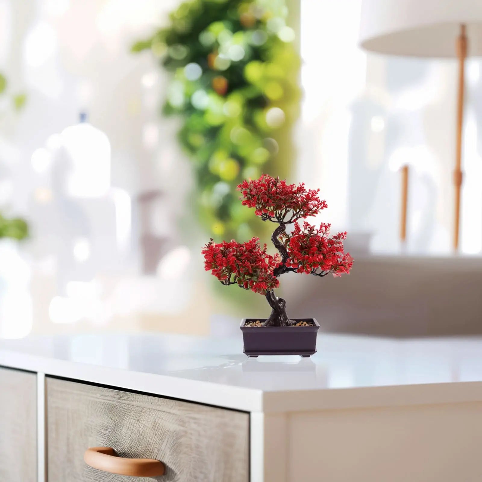 Artificial bonsai tree with vibrant red leaves and a dark twisted trunk in a small black rectangular pot on a desk.