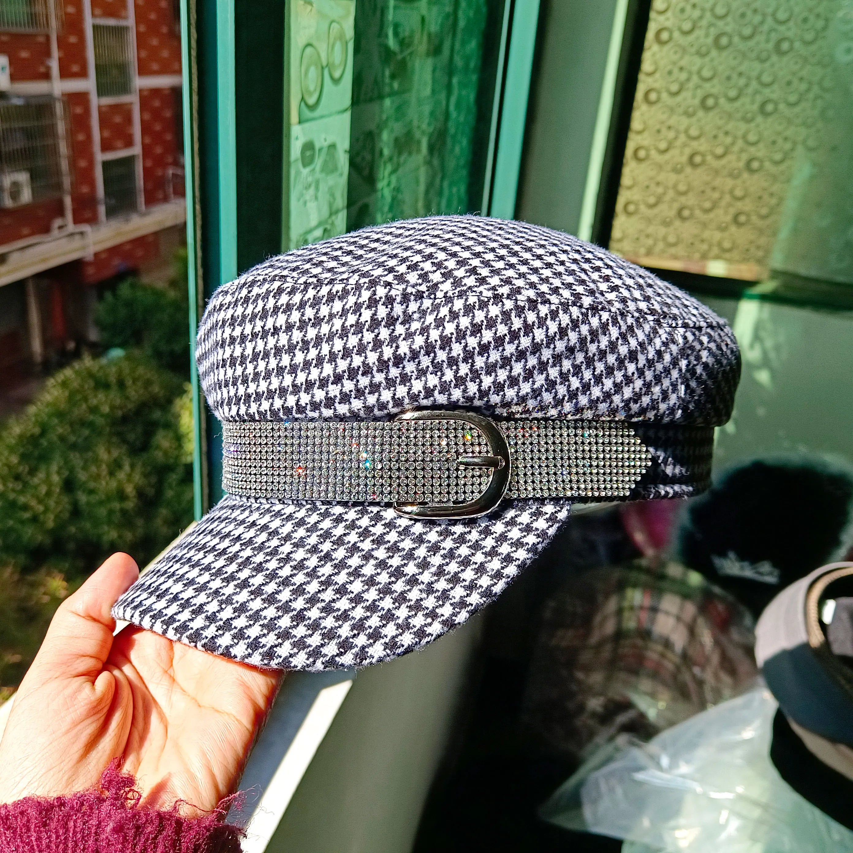 Black and white houndstooth baker boy cap featuring a sparkling rhinestone-embellished band with a silver buckle.