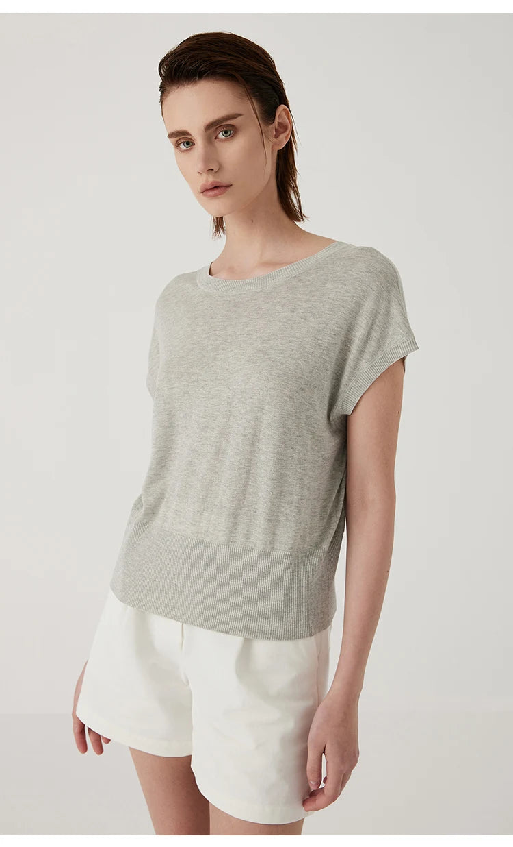 Model wearing a light grey, short-sleeved fine knit top with a round neck and ribbed hem, paired with white shorts.