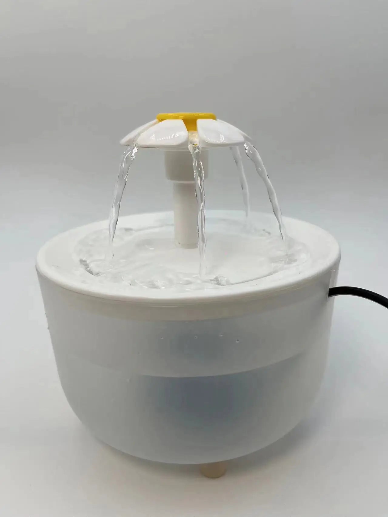 White plastic pet water fountain with a yellow daisy-shaped spout streaming water into a round bowl.