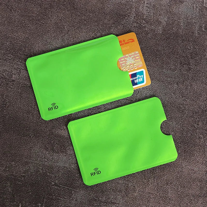 Two bright green RFID-blocking plastic card sleeves, one containing a gold credit card, against a dark textured surface.