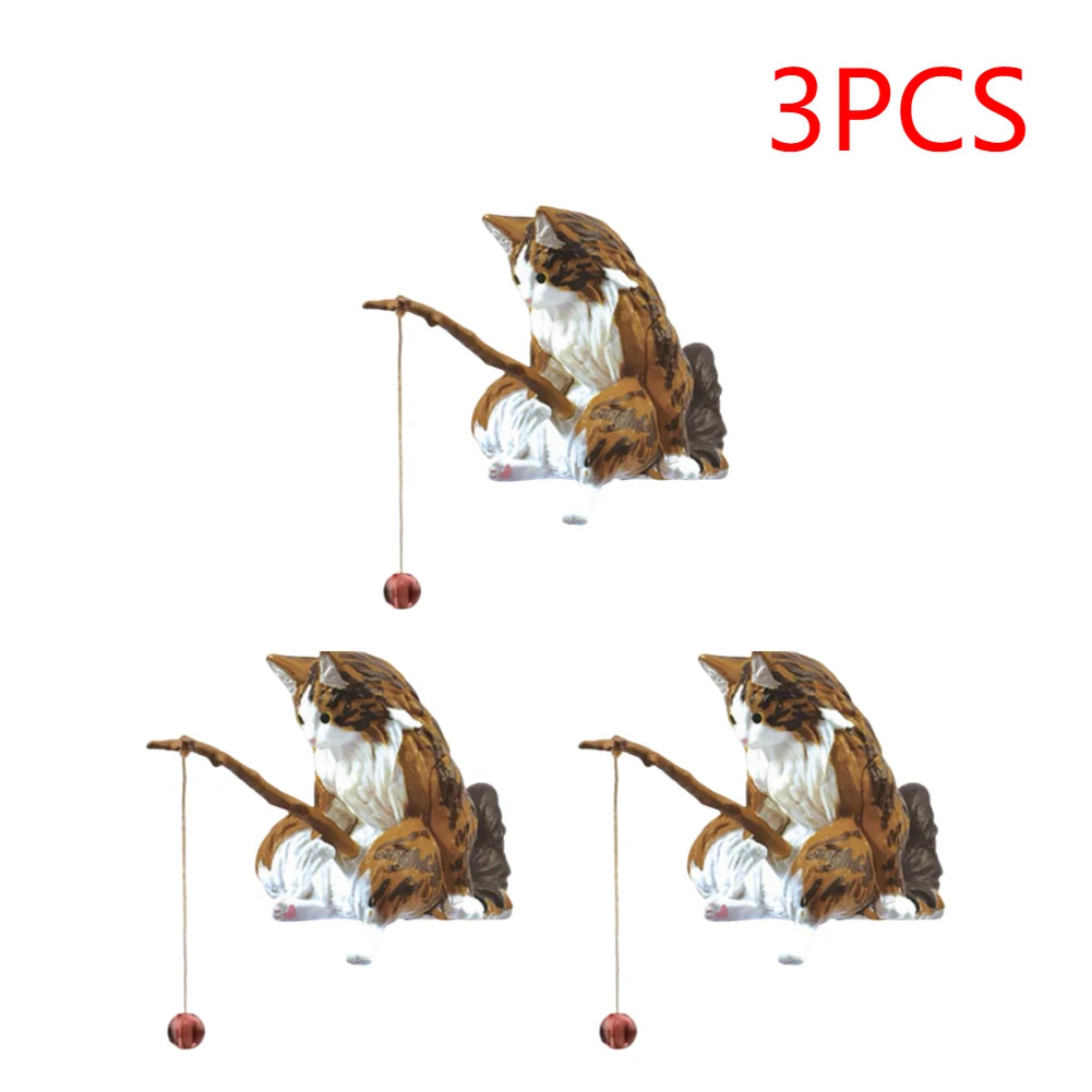 Three brown and white tabby cat aquarium ornaments, each holding a small fishing rod with a hanging bauble.