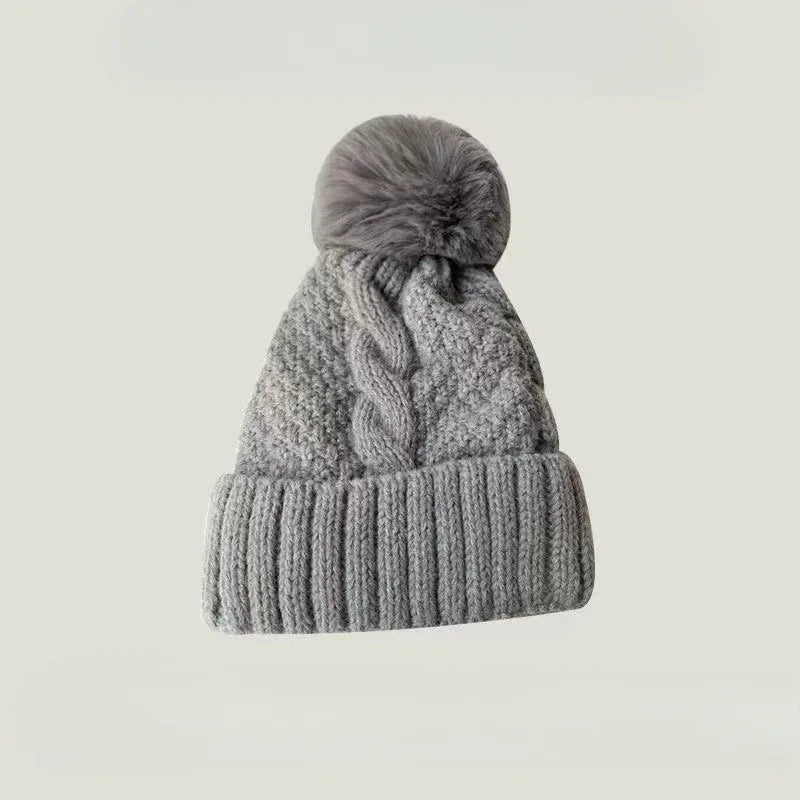 Grey knitted winter beanie hat with a cable knit pattern, ribbed cuff, and a fluffy faux fur pom pom.
