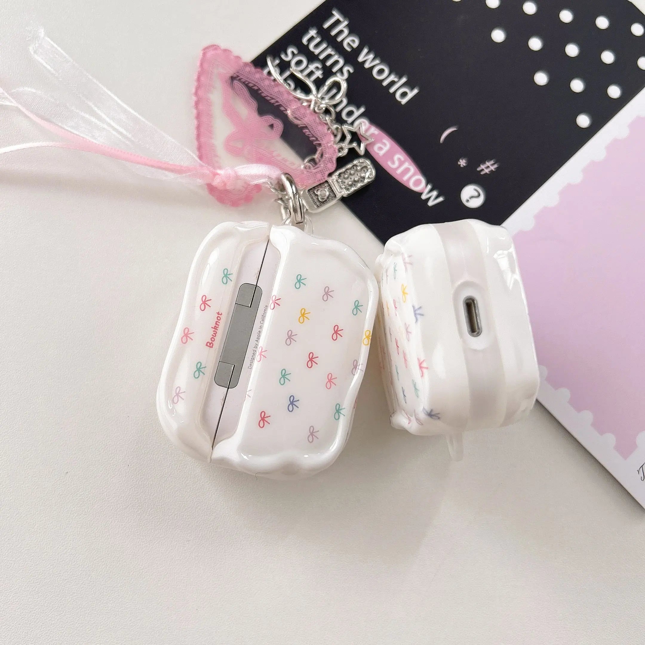 Glossy white AirPods Pro case featuring a colourful bow print and pink ribbon charm.