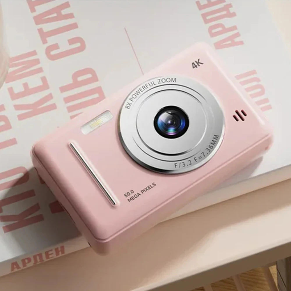 Small pink plastic digital camera with a silver lens, 4K resolution, 8x zoom, and 50MP sensor on a printed surface.