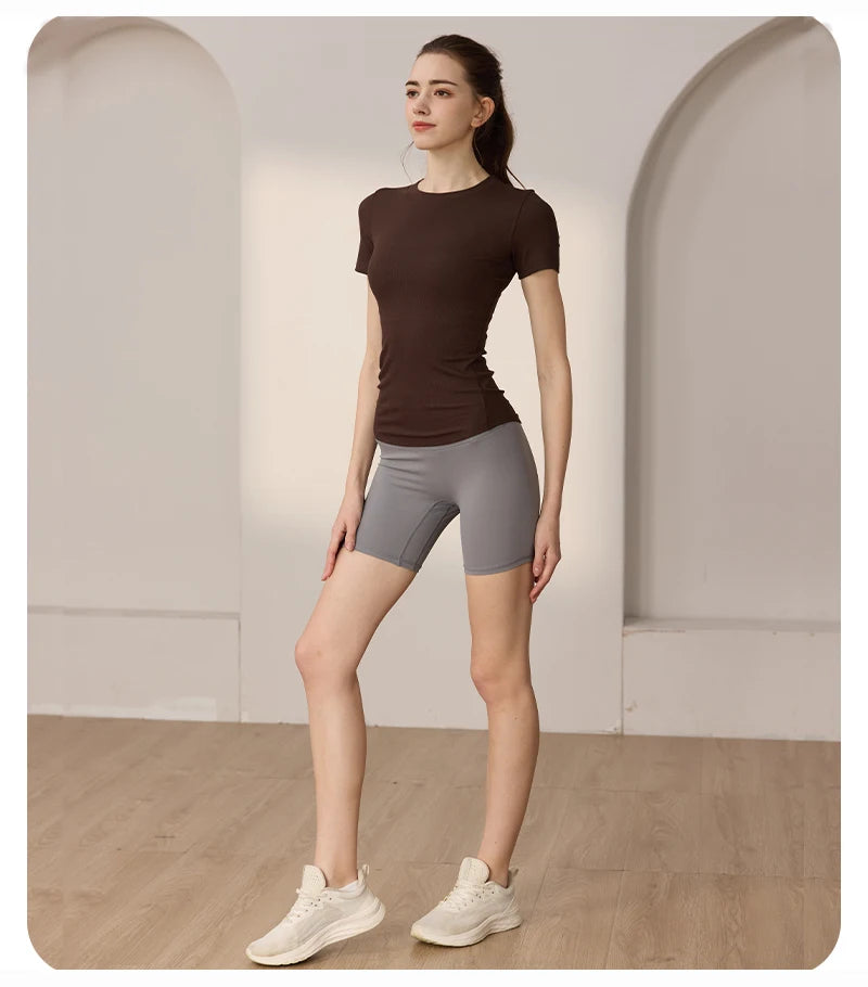 A woman wears a brown ribbed short-sleeve top and grey fitted athletic shorts, perfect for activewear.
