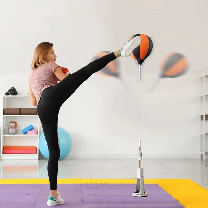 Woman in workout gear kicks an orange and black speed bag on an adjustable stand.