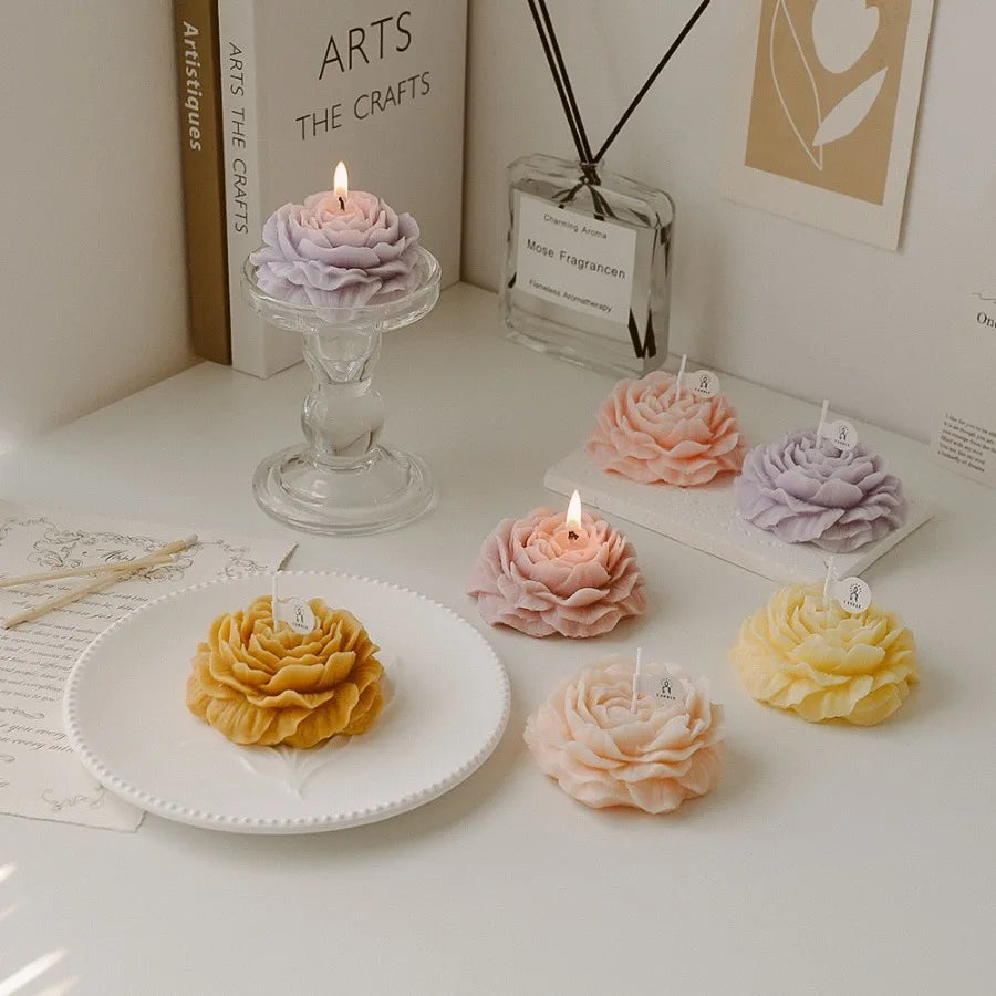 Collection of pastel-coloured, peony-shaped decorative candles arranged on a table with a glass candle holder.