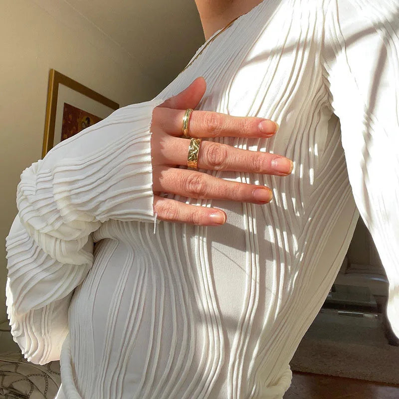 Close-up of a white, long-sleeved, vertically pleated top with textured fabric detail.