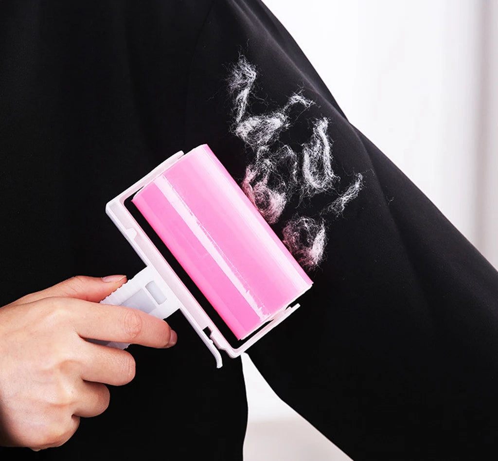 A person using a pink, sticky lint roller to remove white fluff from a black sleeve.