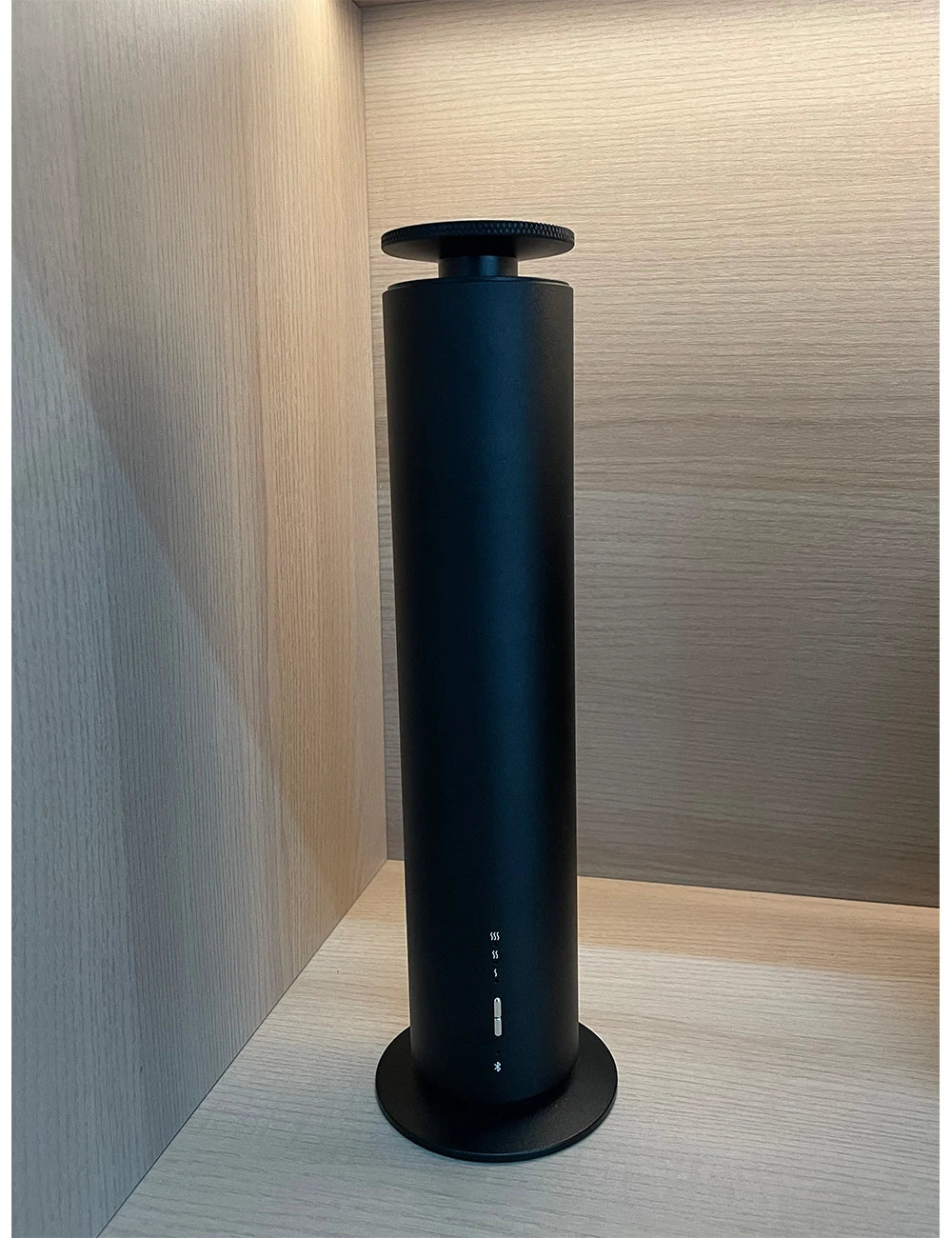 Sleek, black cylindrical smart aroma diffuser standing on a light wood shelf with minimalist touch controls.