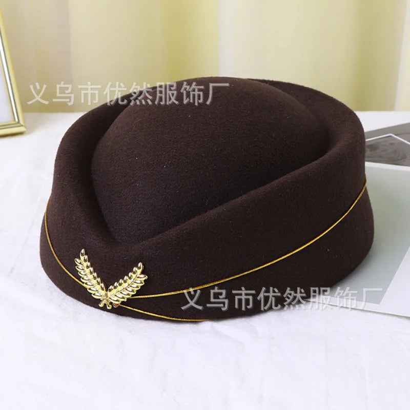 Dark brown vintage-style pillbox hat featuring gold trim and a metallic leaf emblem on the front.