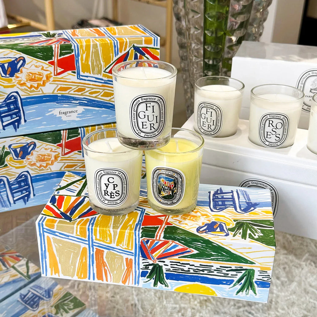 A collection of scented candles in clear glass jars, presented in a decorative box with a vibrant summer scene.