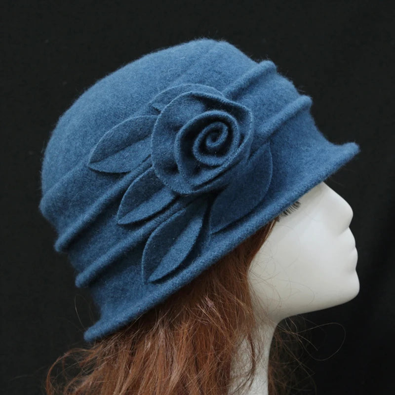 Elegant blue wool cloche-style hat featuring a felt rose and leaf embellishment, shown on a mannequin.