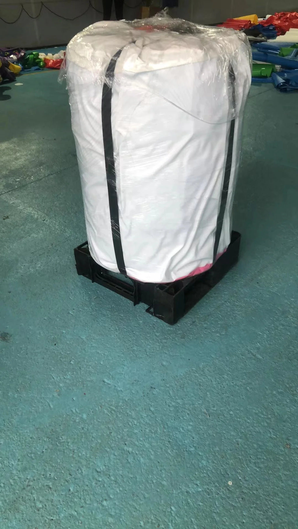 Large white industrial bulk bag with black straps, shrink-wrapped and secured on a black plastic pallet.