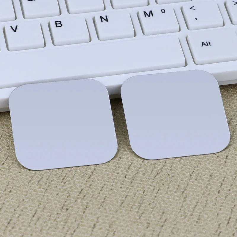 Two blank, square, light grey adhesive stickers placed on a textured surface in front of a white computer keyboard.