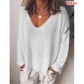 Woman wearing a loose-fit white long-sleeve jumper with a deep V-neckline and dropped shoulders.