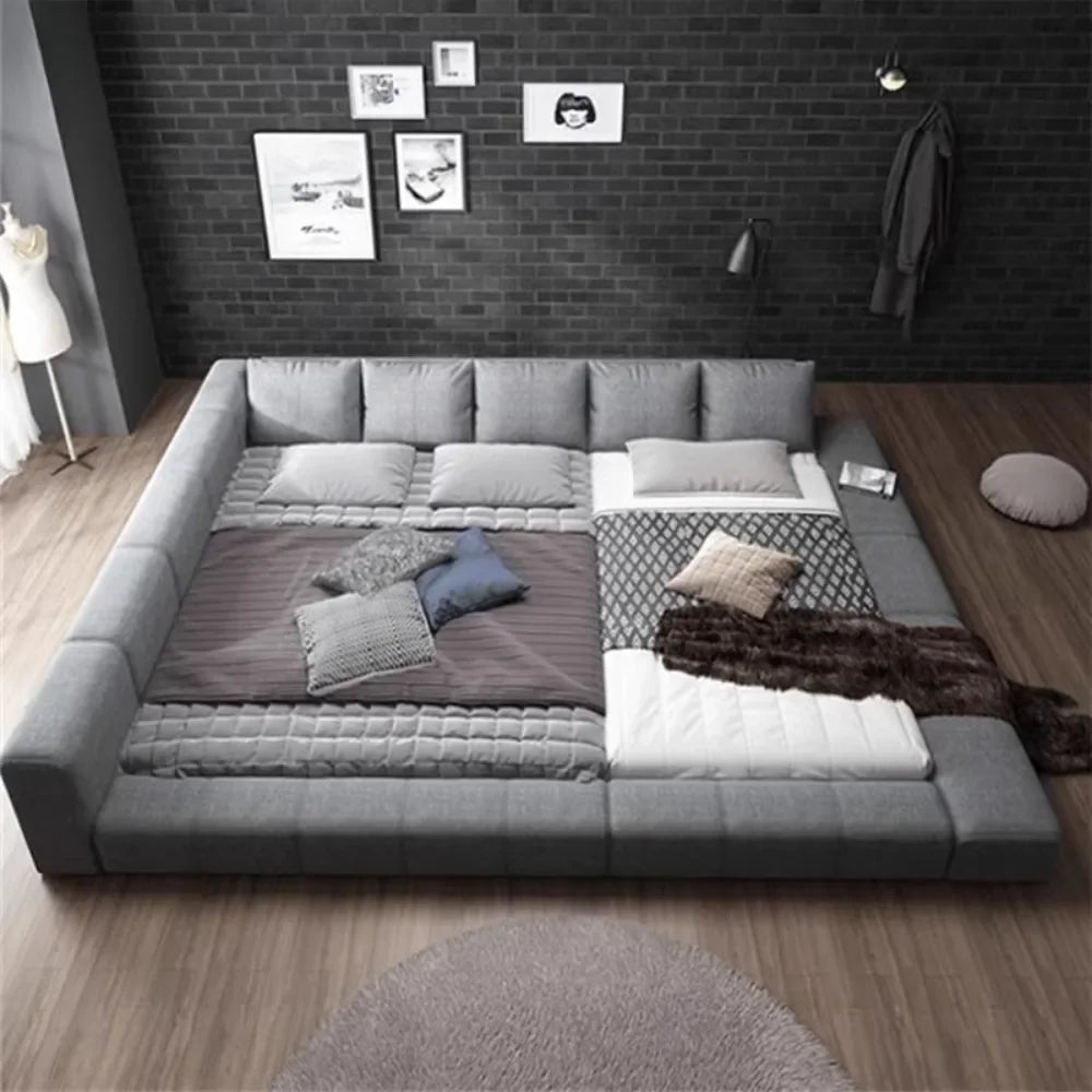 Modern grey upholstered low-profile double bed with a wide padded frame and integrated headboard cushions.