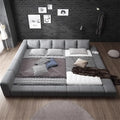 Modern grey upholstered low-profile double bed with a wide padded frame and integrated headboard cushions.