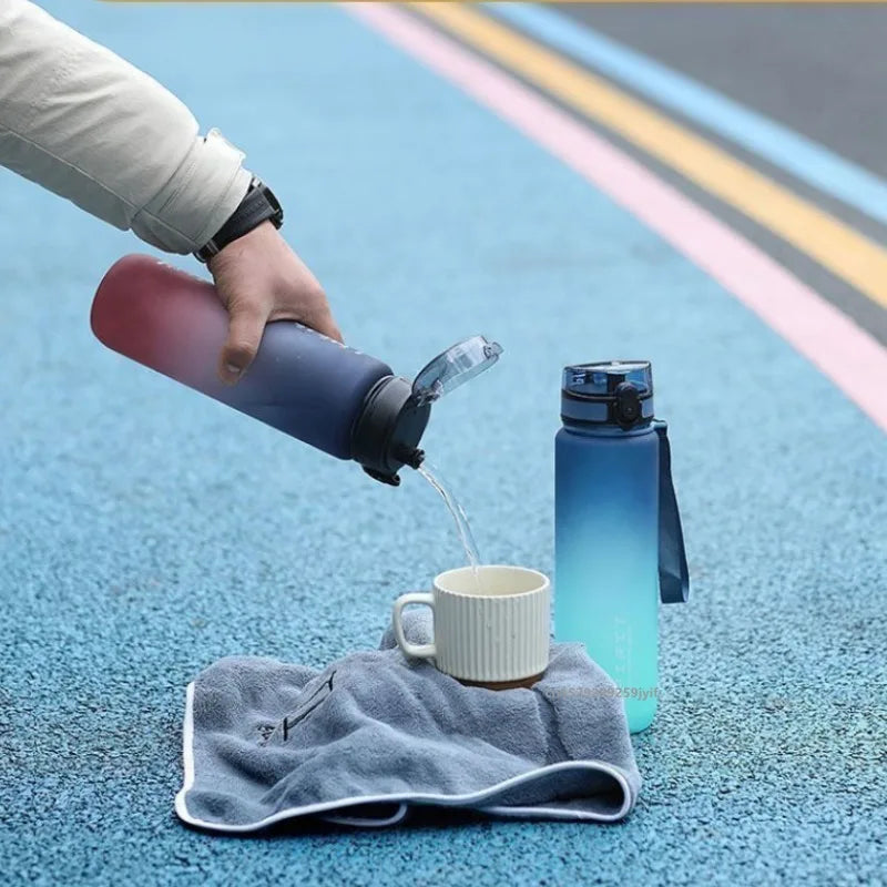 A hand pours water from a pink-to-navy ombre sports bottle into a small, ribbed cream mug on a grey towel.