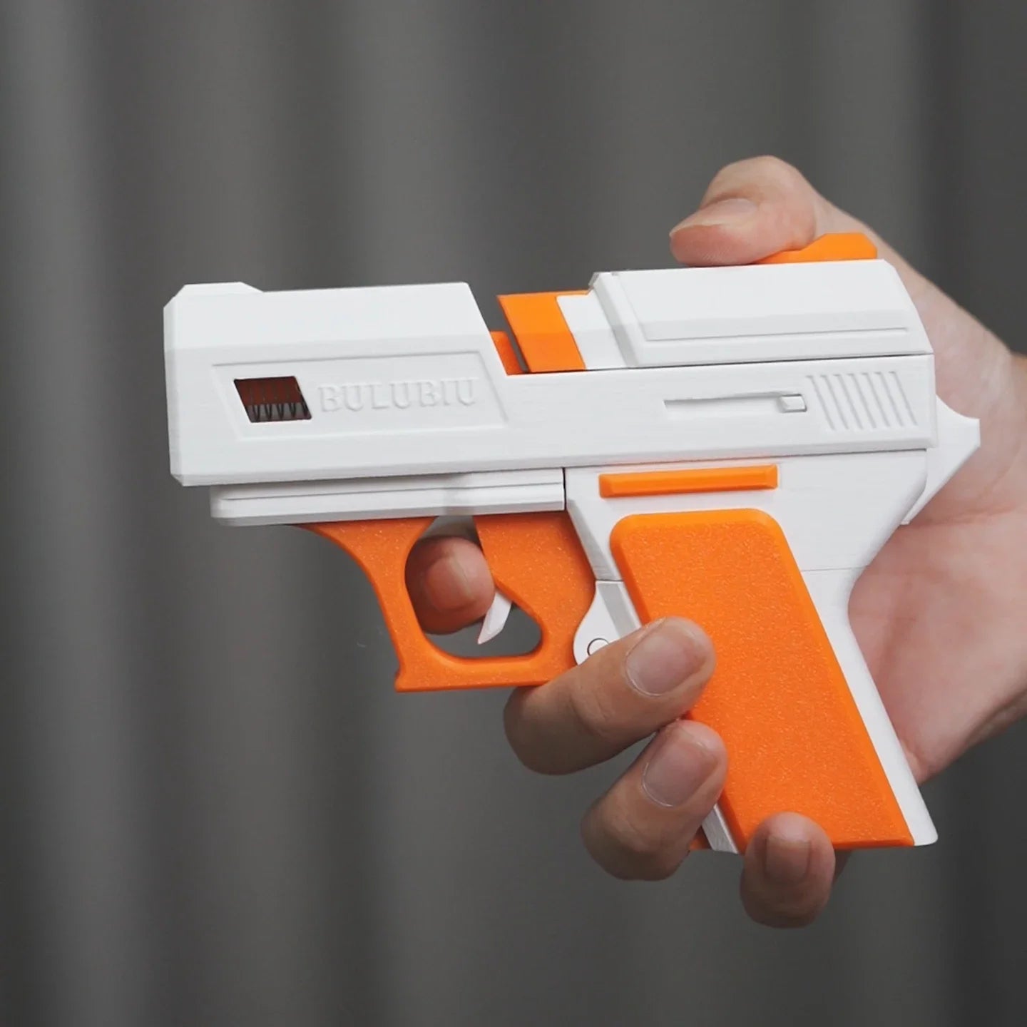 Handheld white and orange gun-style AirPods case made of hard plastic, held in a hand against a grey background.