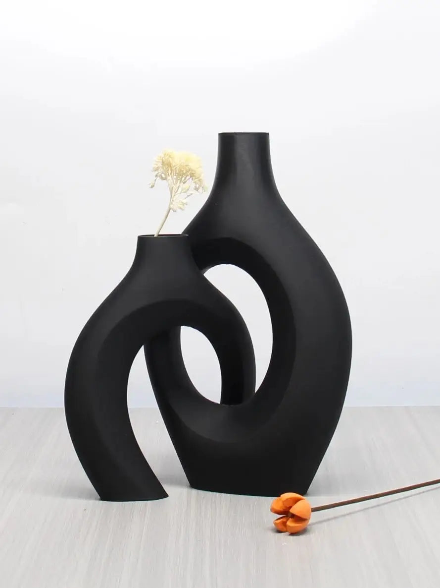 Two interlocking matte black ceramic vases with a bohemian, sculptural design and cut-out centres.