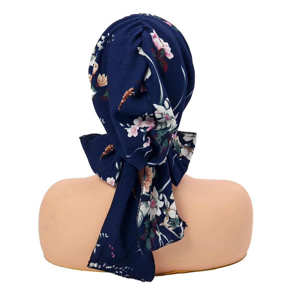 Vintage-style navy turban hat with a floral pattern and a decorative tie-brim, shown from the back on a mannequin.