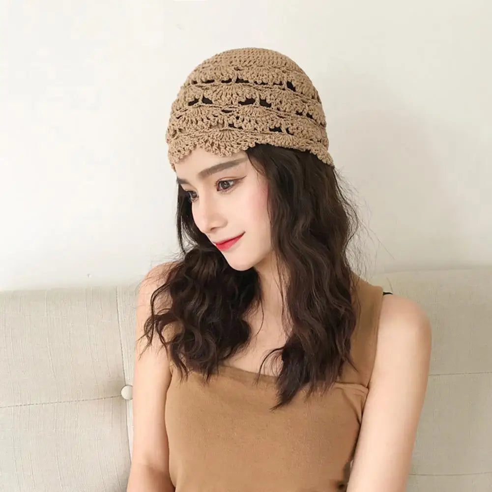 A woman wears a beige, hollow-crochet lace beanie with a delicate scalloped edge and textured floral pattern.