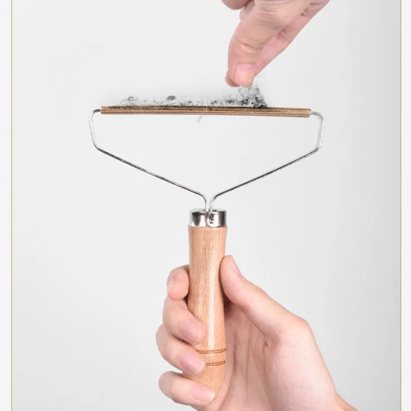 Handheld lint remover tool with a wooden handle and metal scraper head, showing lint collected along the edge.