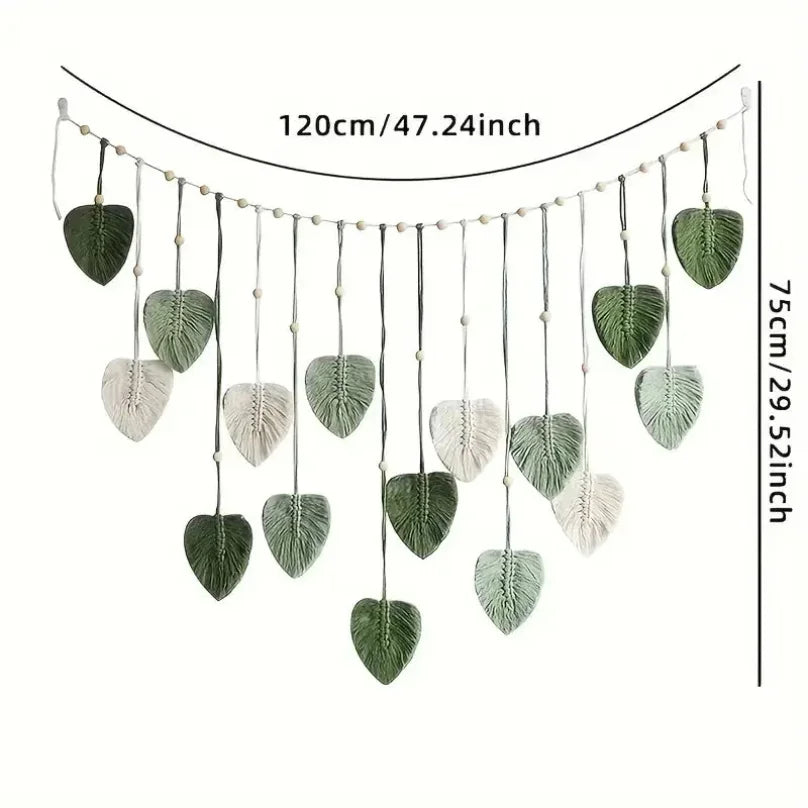 Boho-style macrame wall hanging featuring sage green and cream leaf motifs on a beaded cord garland.