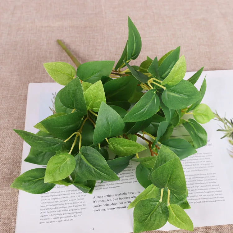 A bunch of artificial green leaves with varying shades and yellow-green stems lying on a printed book.