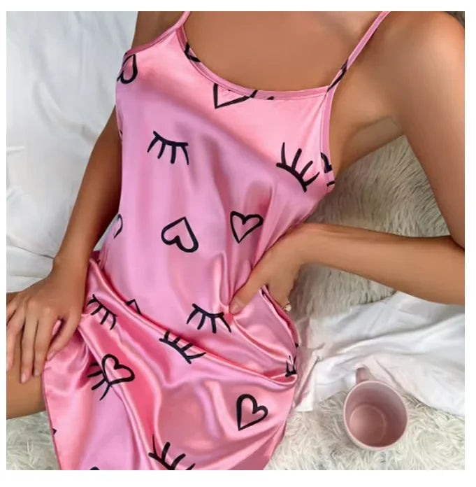 Pink satin camisole nightdress with black eyelash and heart print, featuring delicate spaghetti straps.